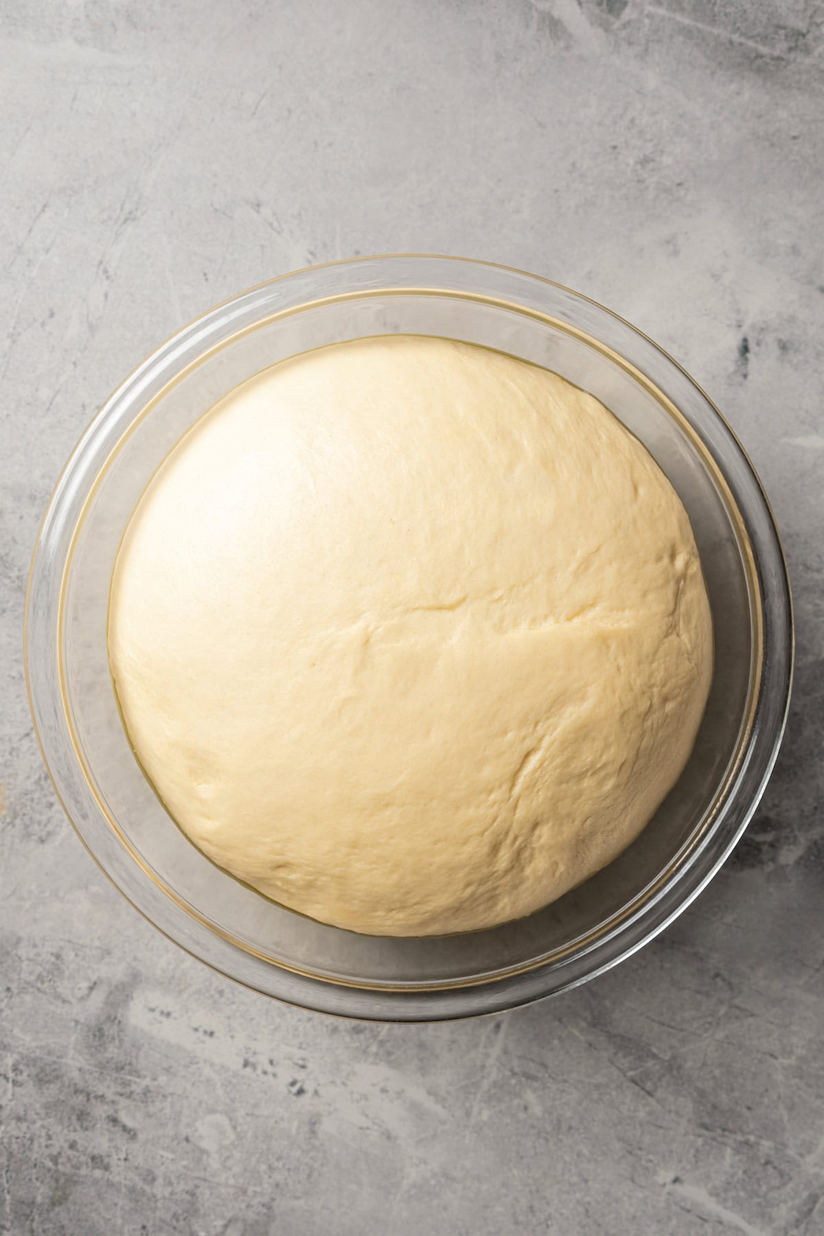 Dinner roll dough after rising inside a glass bowl.