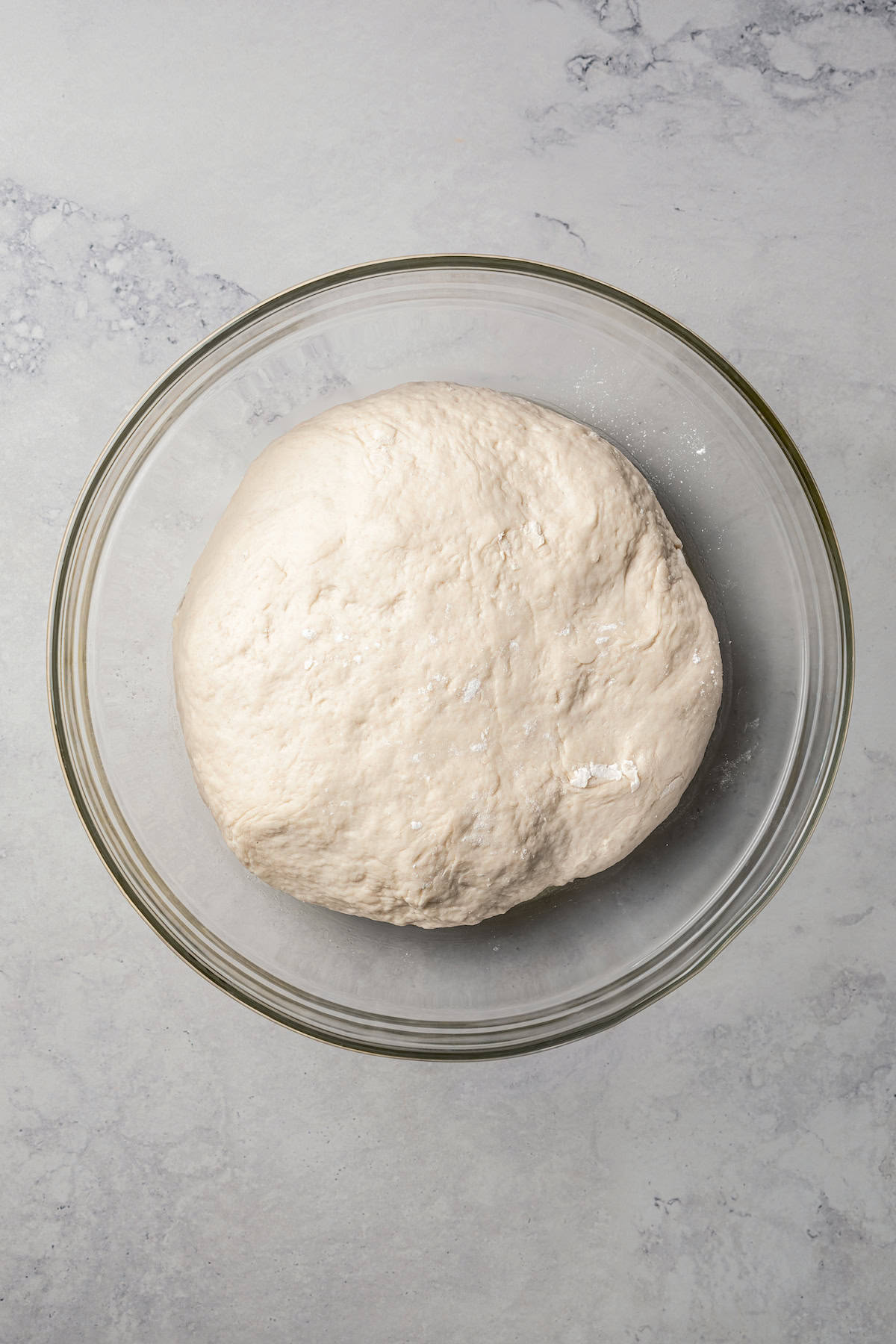 A ball of bagel dough inside a glass bowl.