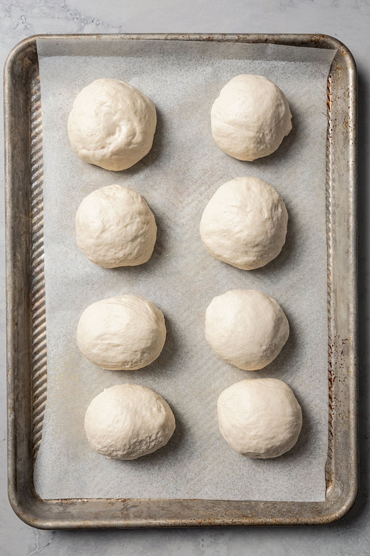 Bagel dough portioned out into balls on a lined baking sheet.