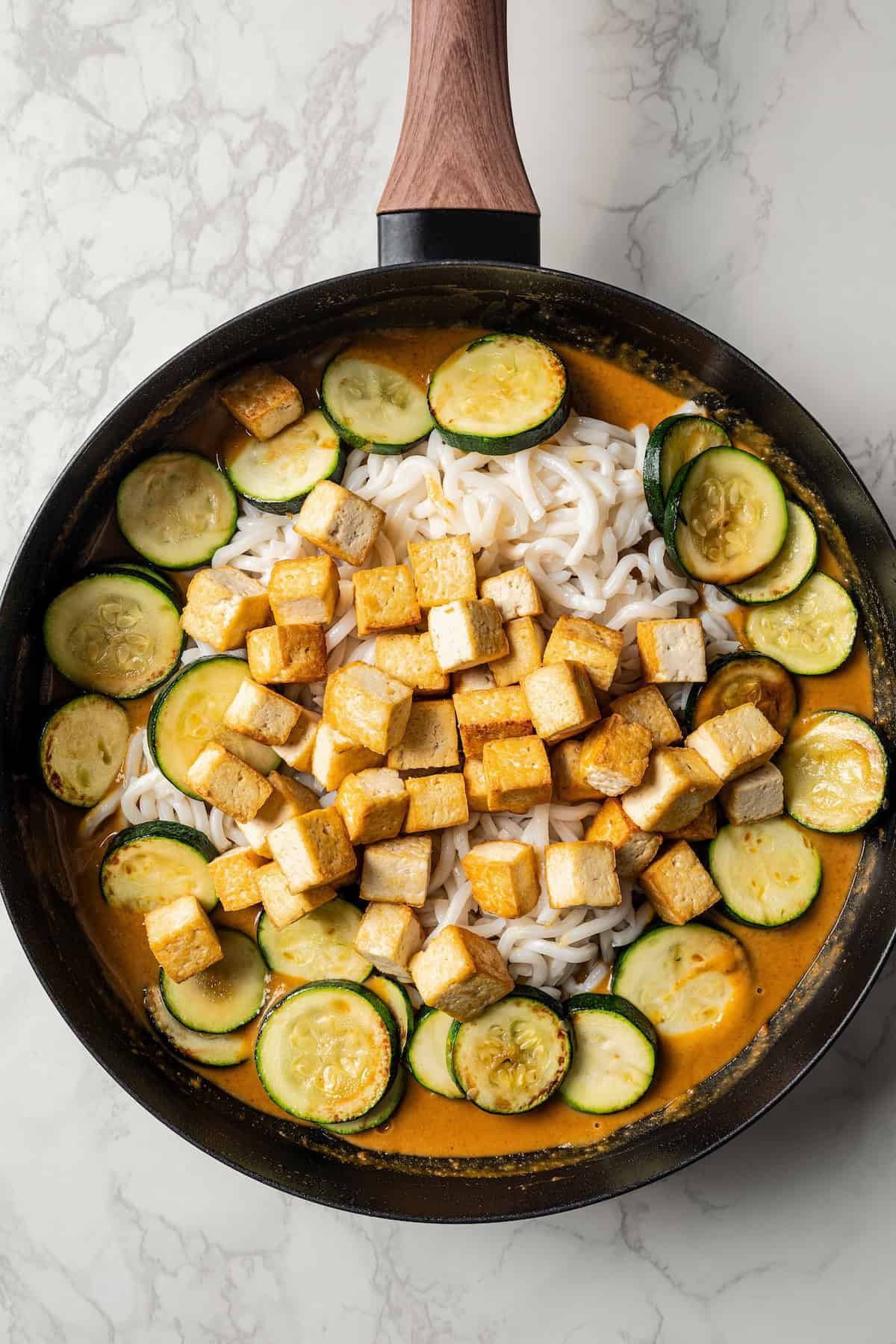 Adding cooked tofu and zucchini to the noodles with peanut sauce.