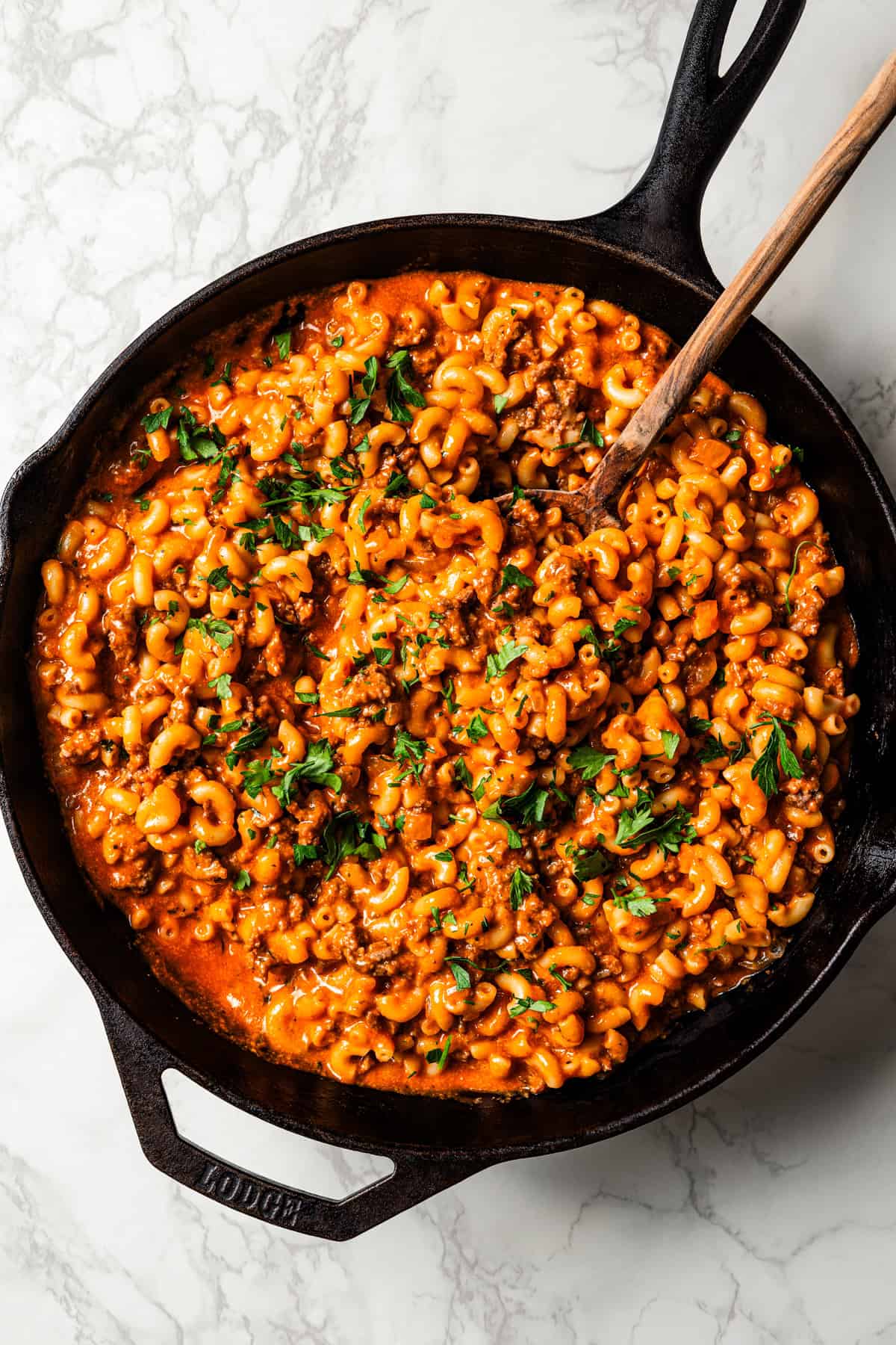 Overhead view of beefaroni in a large skillet with a wooden serving spoon resting in it.