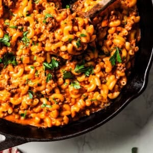 Beefaroni in a large skillet with a wooden serving spoon stirring through it.