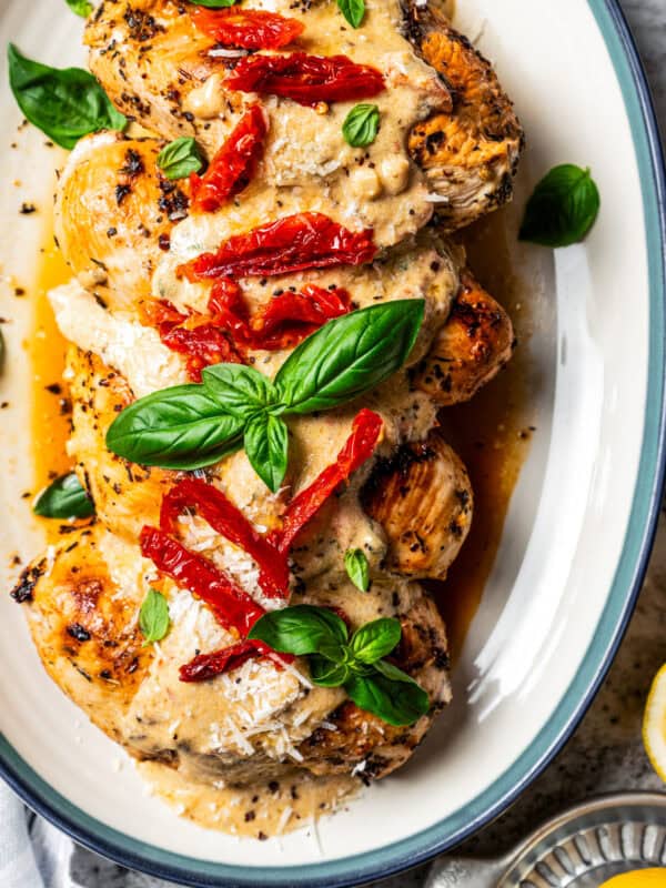 Overhead view of Chicken Bryan topped with creamy lemon butter sauce, sun-dried tomatoes, and basil on a platter.