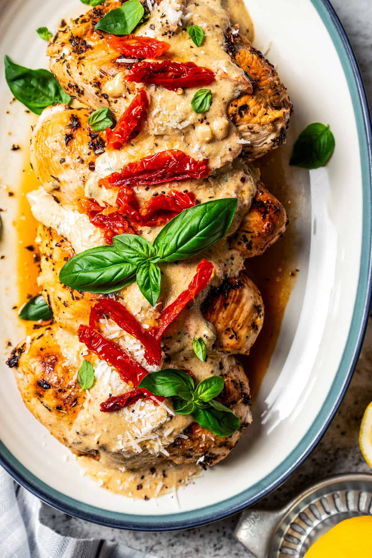 Overhead view of Chicken Bryan topped with creamy lemon butter sauce, sun-dried tomatoes, and basil on a platter.