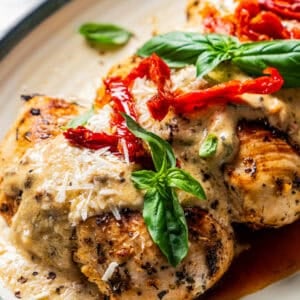 Close up of Chicken Bryan topped with creamy lemon butter sauce, sun-dried tomatoes, and basil on a platter.