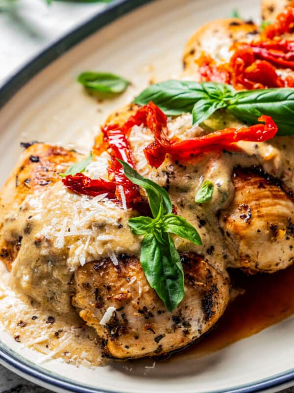 Close up of Chicken Bryan topped with creamy lemon butter sauce, sun-dried tomatoes, and basil on a platter.