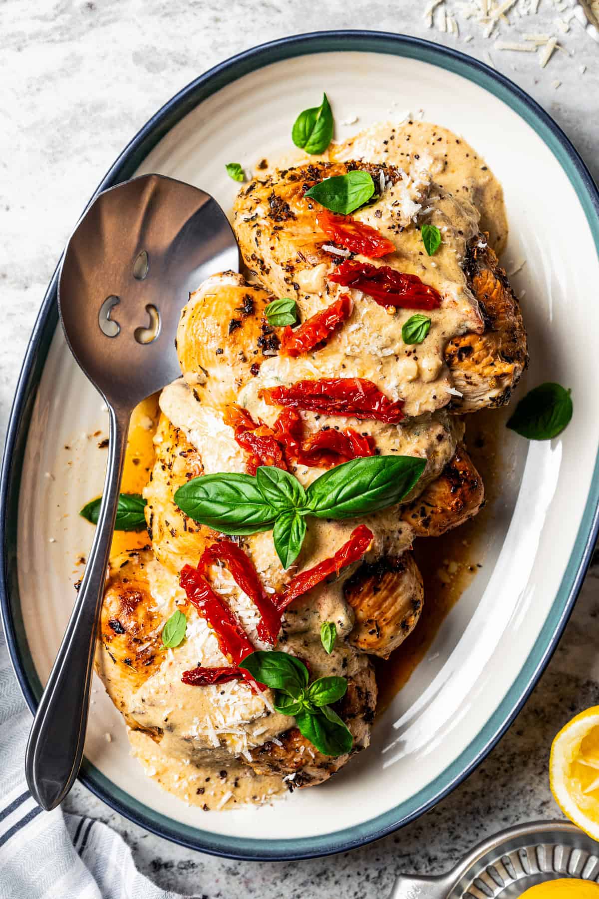 Chicken Bryan topped with creamy lemon butter sauce, sun-dried tomatoes, and basil on a platter with a spoon for serving.