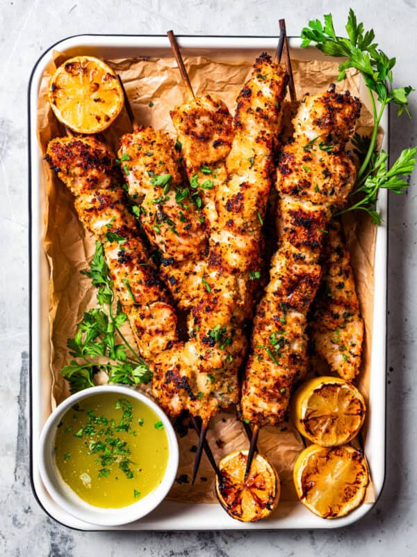 Chicken spiedini skewers are on a metal tray lined with parchment paper, and a bowl of lemon butter sauce is also on the tray.