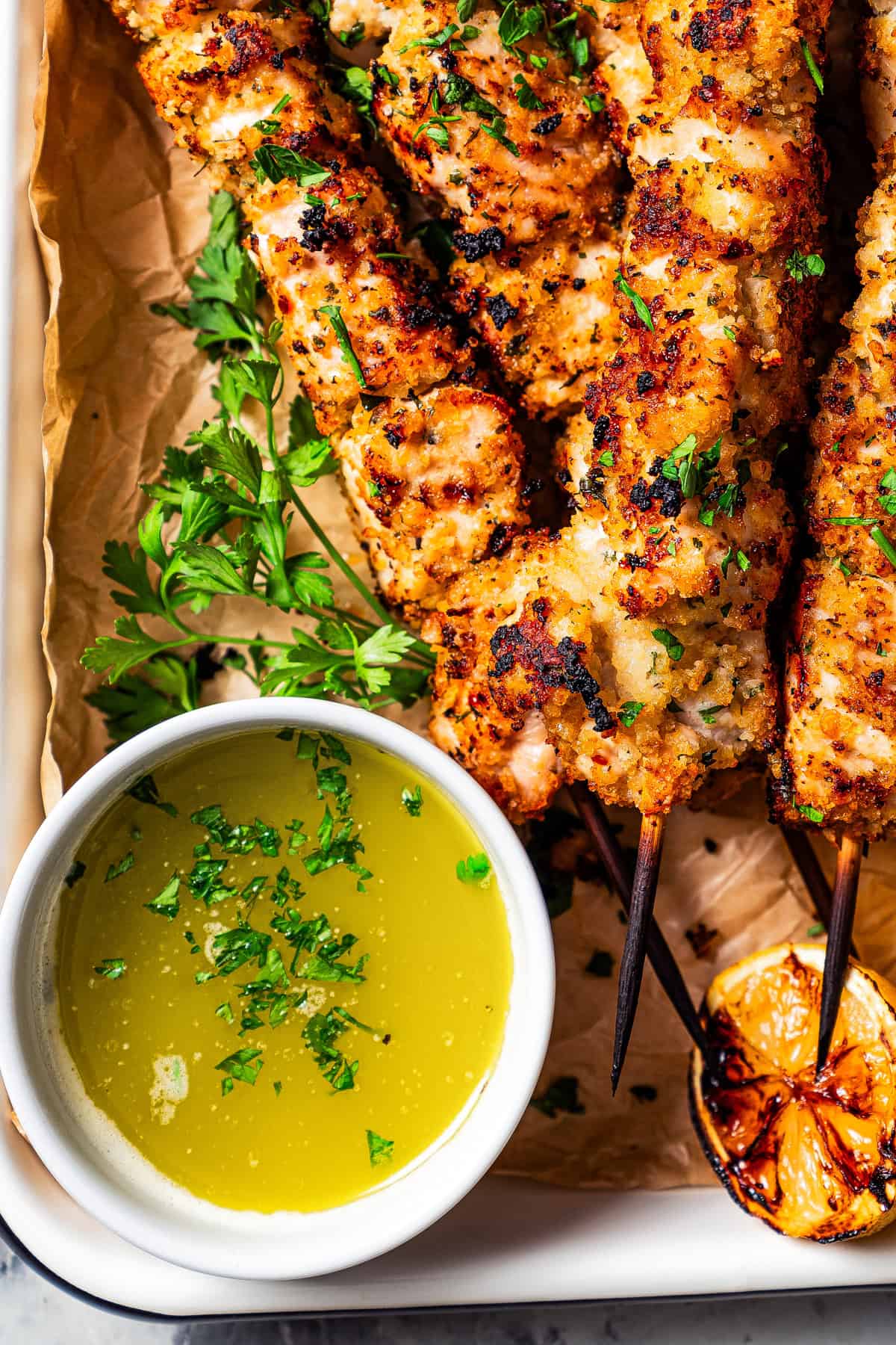 A bowl of lemon butter sauce served next to skewers with chicken.