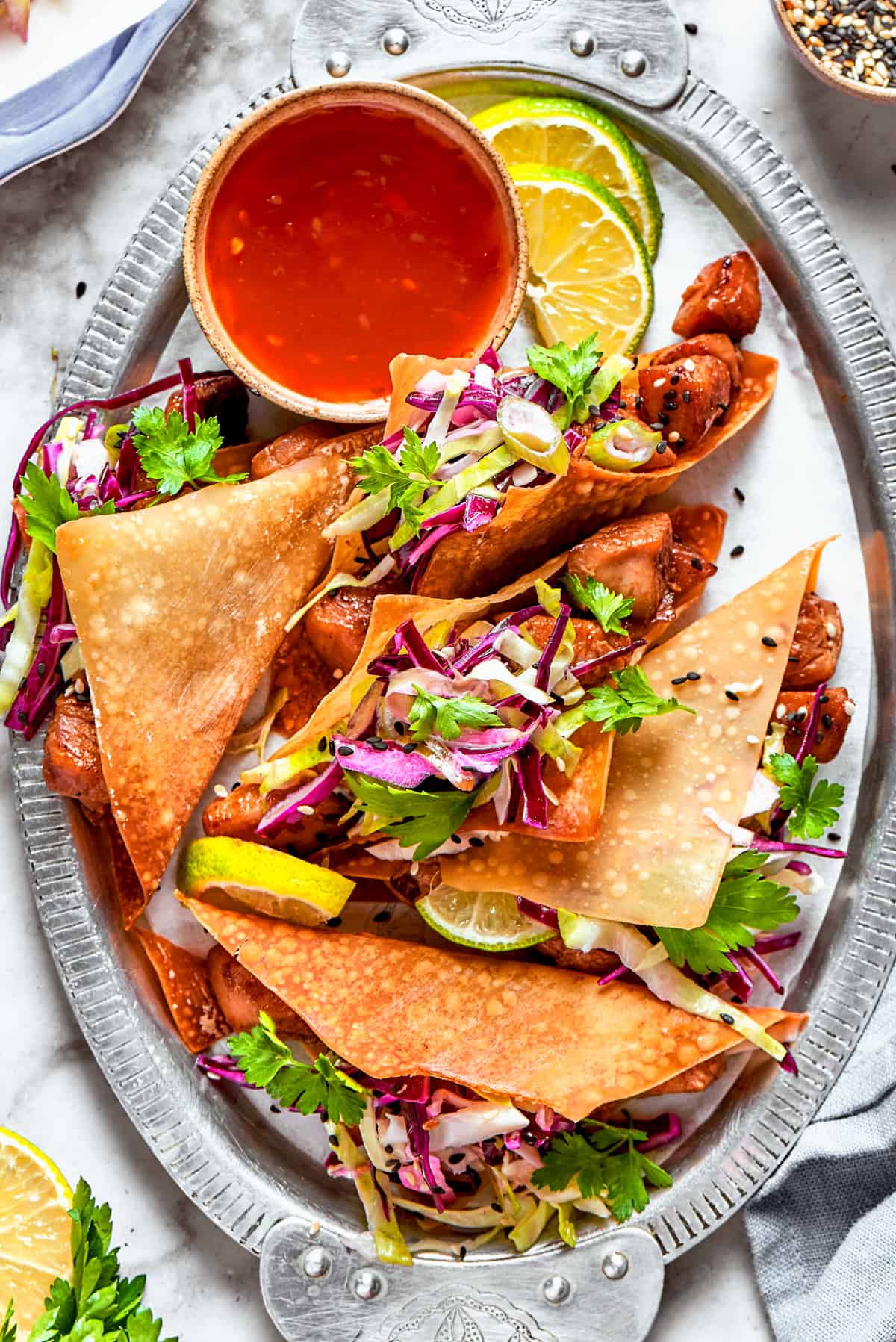 Chicken Wonton Tacos arranged on a plate with a bowl of dipping sauce placed next to them.