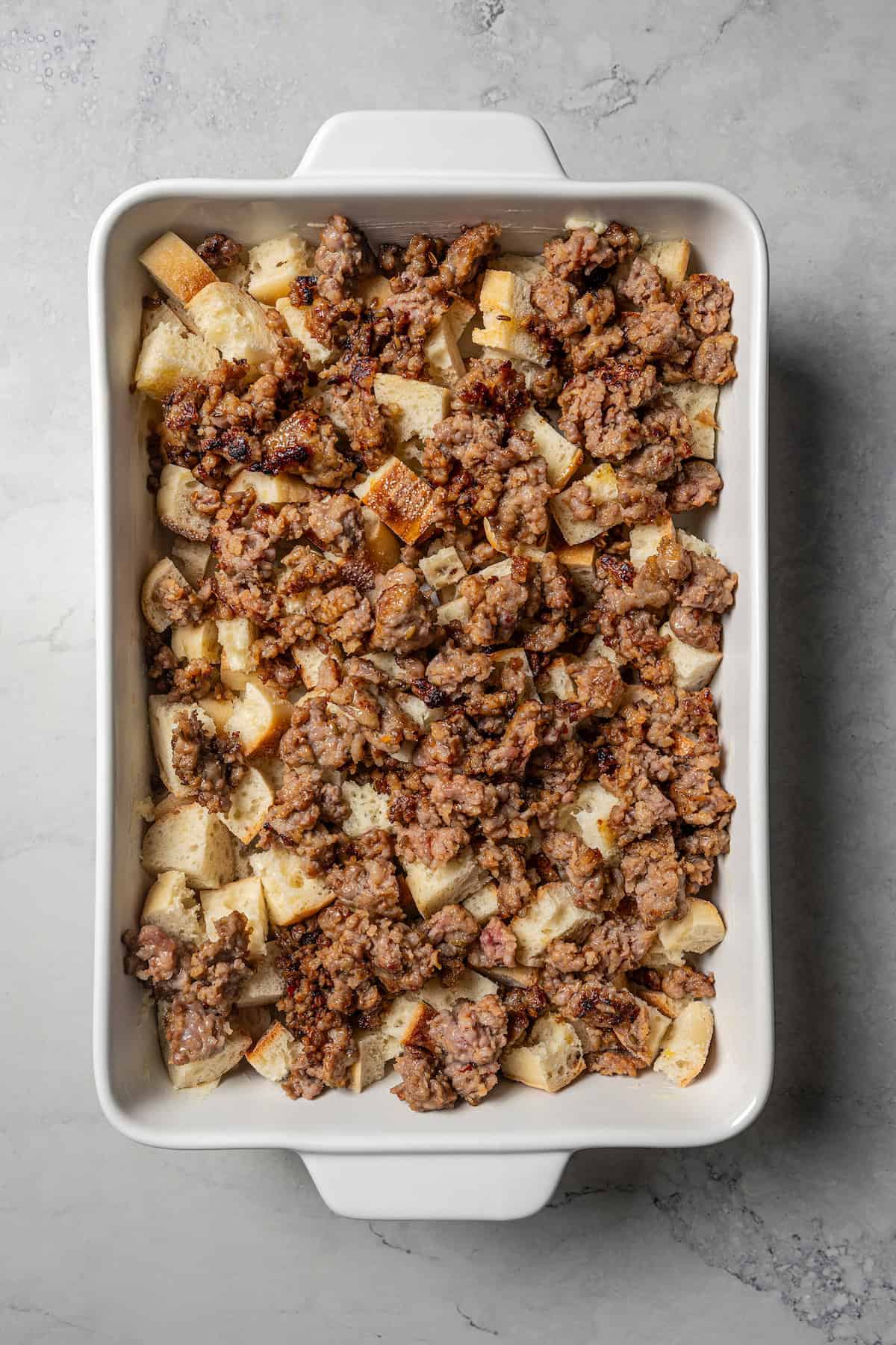 Browned sausage layered over bread cubes in a baking dish.