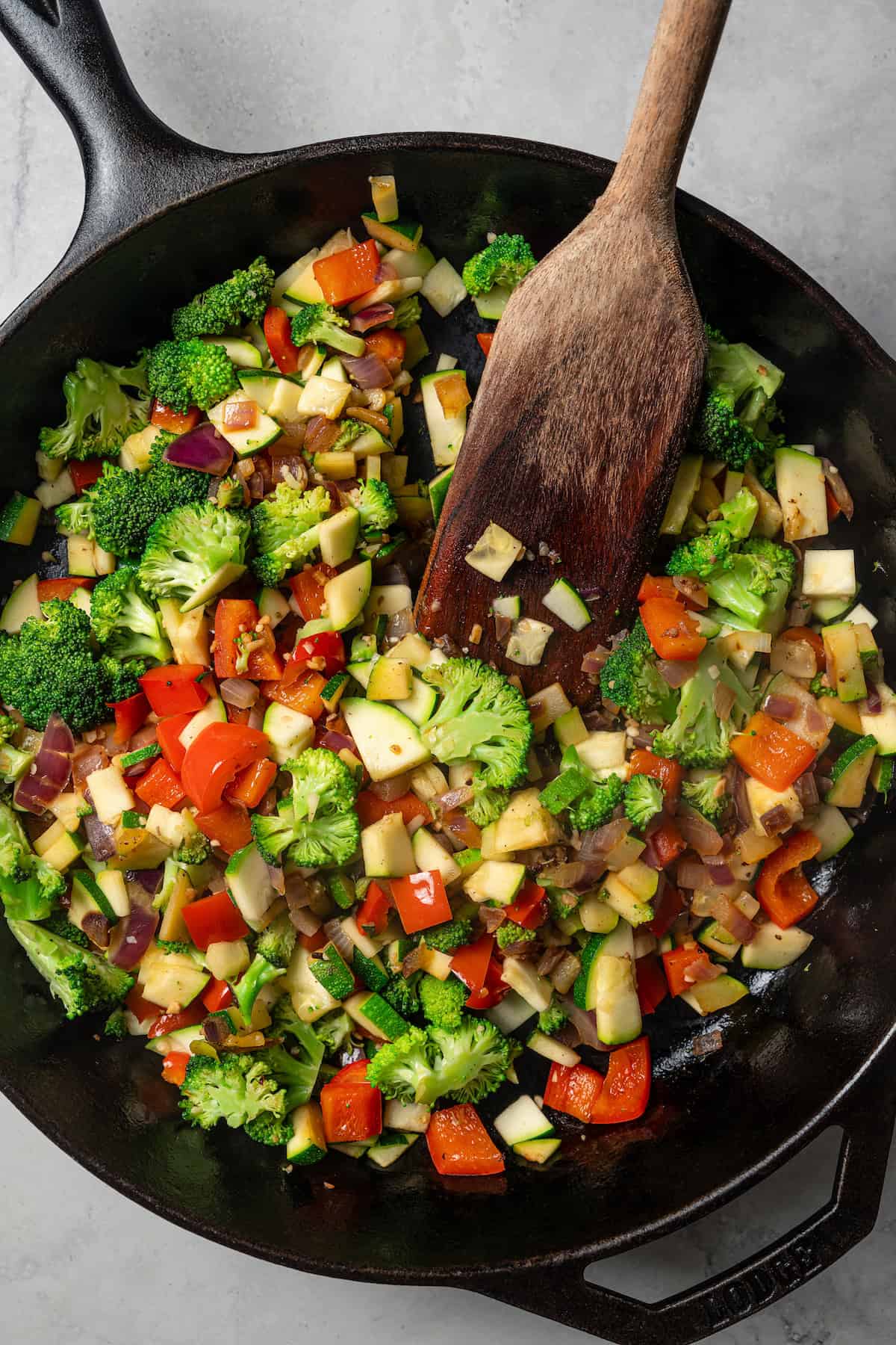 A wooden spoon stirring sautéed diced vegetables in a skillet.