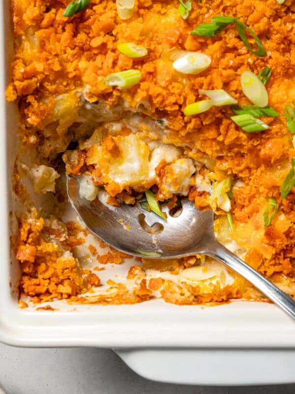 Cheesy funeral potatoes in a baking dish, with a serving spoon scooping them out.