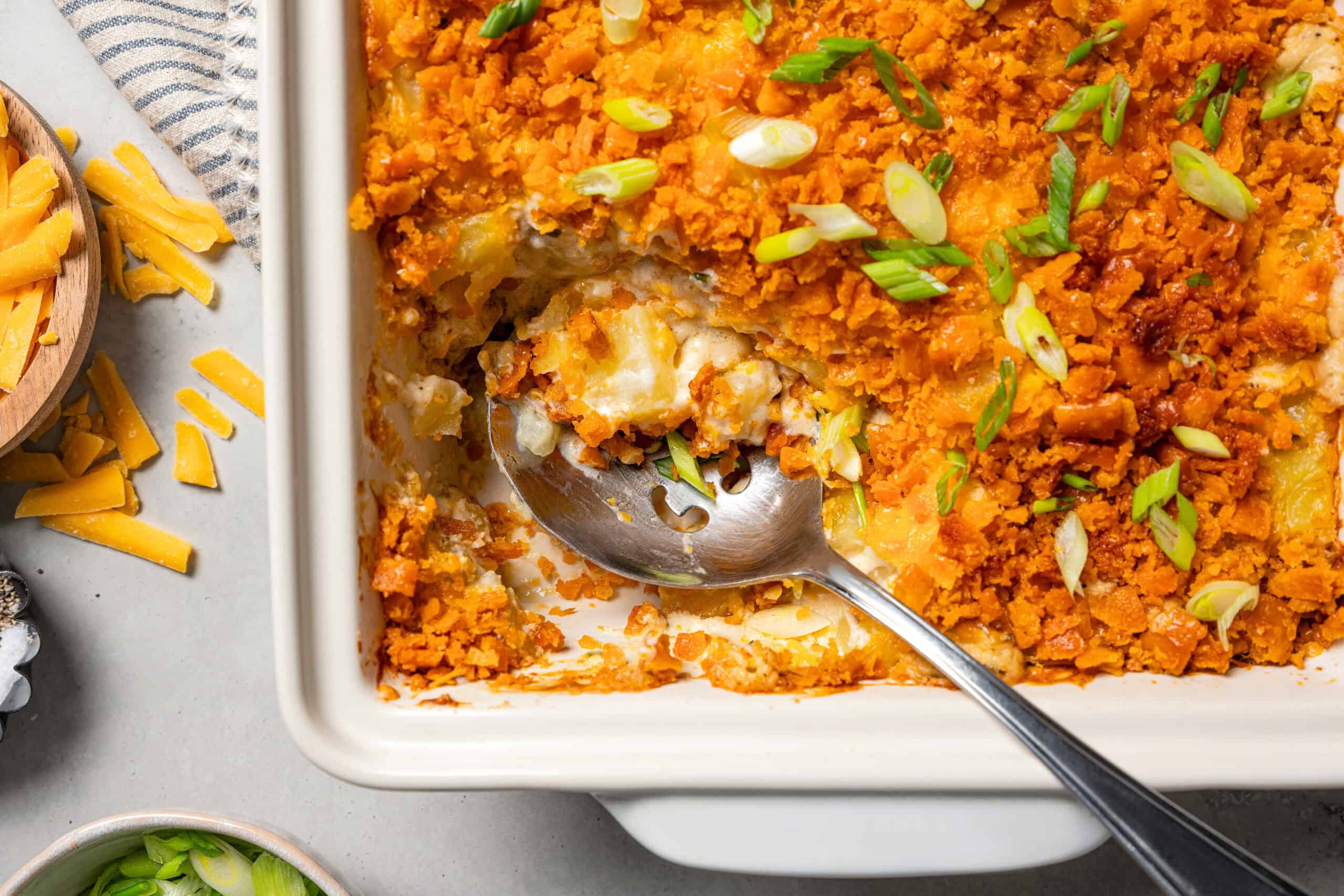 Creamy, golden-baked cheesy potatoes are an easy side dish loaded with potatoes, condensed soup, and cheese topped with a crispy cracker topping. Cheesy funeral potatoes in a baking dish, with a serving spoon scooping them out.