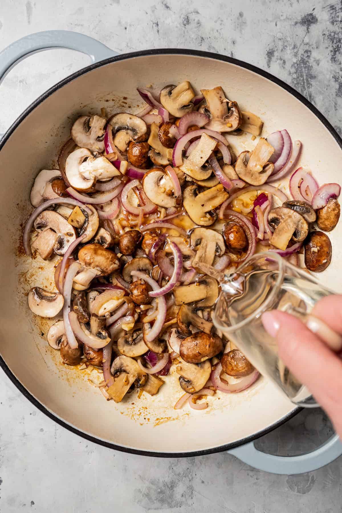 Adding white wine to chicken and mushrooms in a pan.