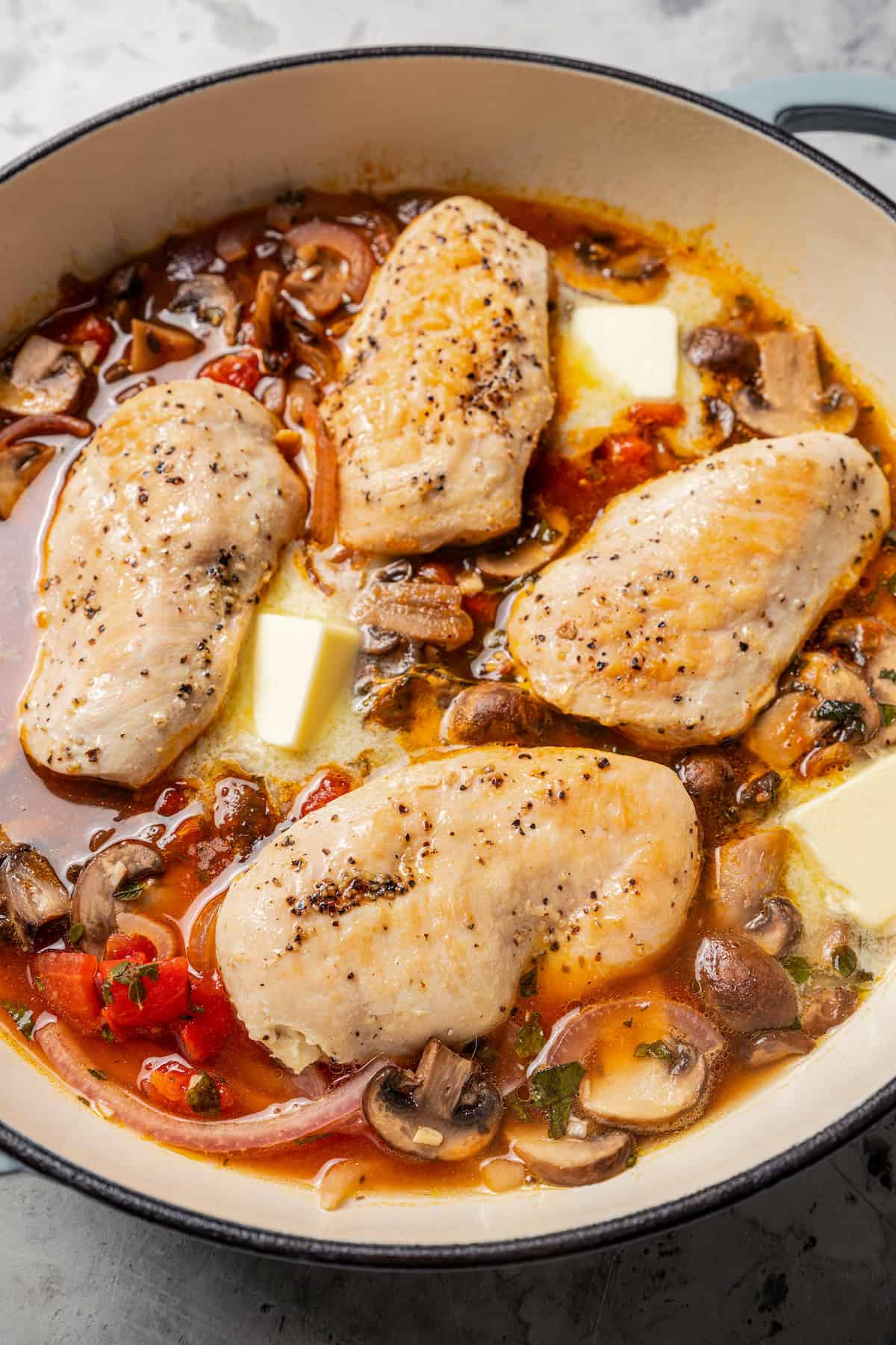 Adding butter and chicken to a pan with sauce.