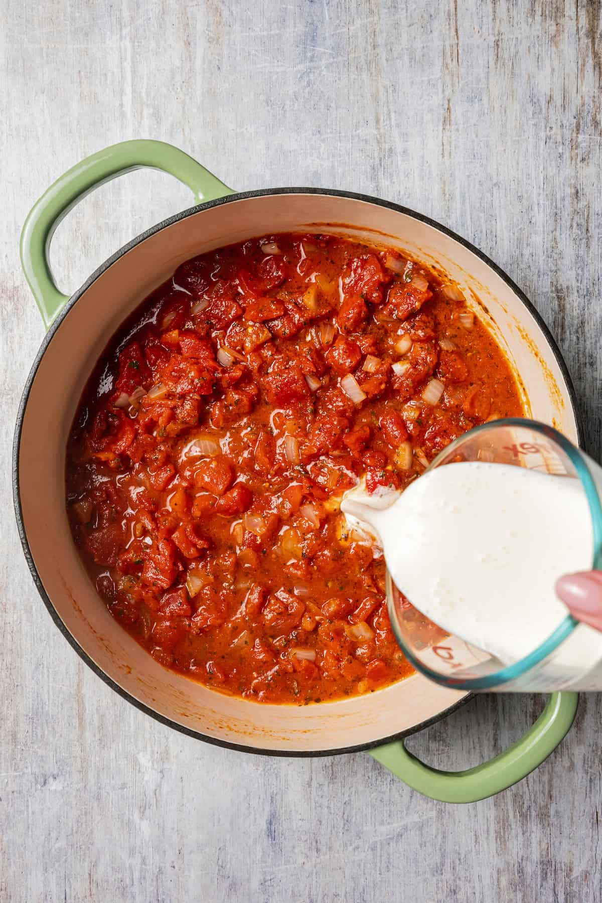 Adding cream to pasta sauce.