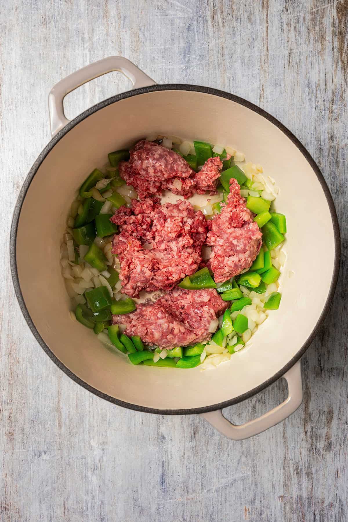 Ground beef added to sauteed bell peppers and onions in a large pot.