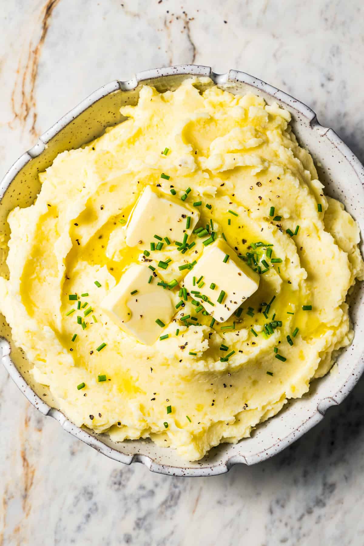 Buttermilk mashed potatoes in a bowl topped with pats of butter and a sprinkle of fresh green herbs.