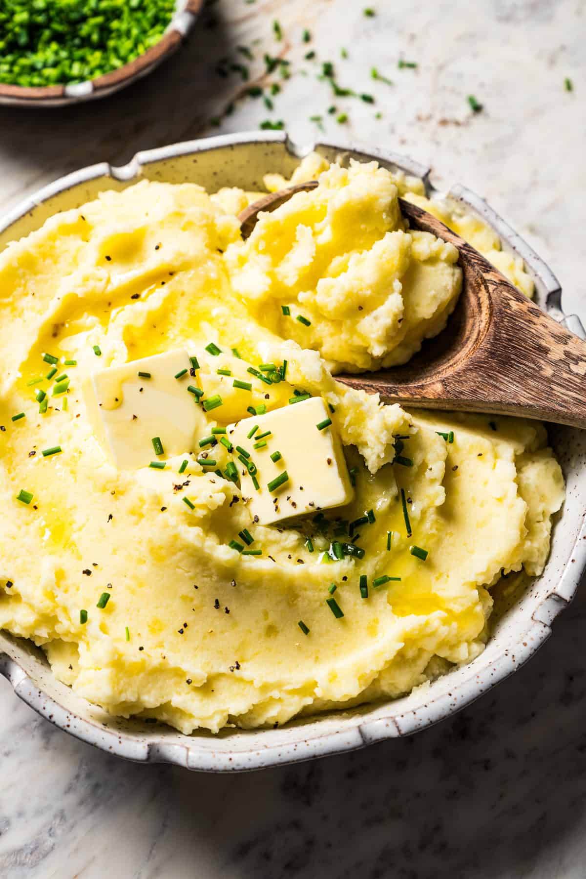 Wooden spoon scooping out mashed potatoes from a bowl.