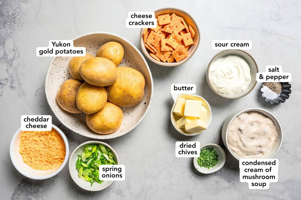 Creamy, golden-baked cheesy potatoes are an easy side dish loaded with potatoes, condensed soup, and cheese topped with a crispy cracker topping. Ingredients for cheesy potatoes arranged on a white surface.