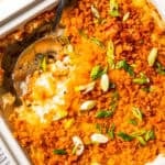 Close-up of cheesy potatoes in a casserole dish with a scoop missing from the corner and a serving spoon resting in the space.
