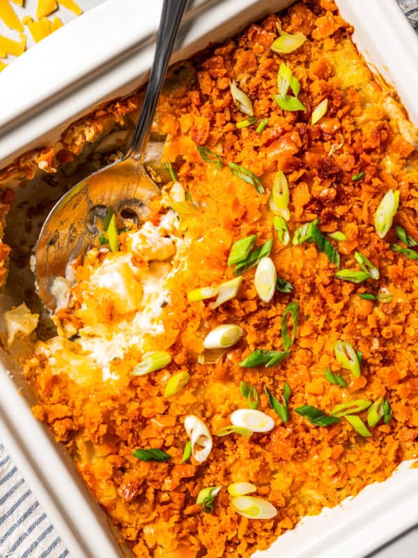 Close-up of cheesy potatoes in a casserole dish with a scoop missing from the corner and a serving spoon resting in the space.