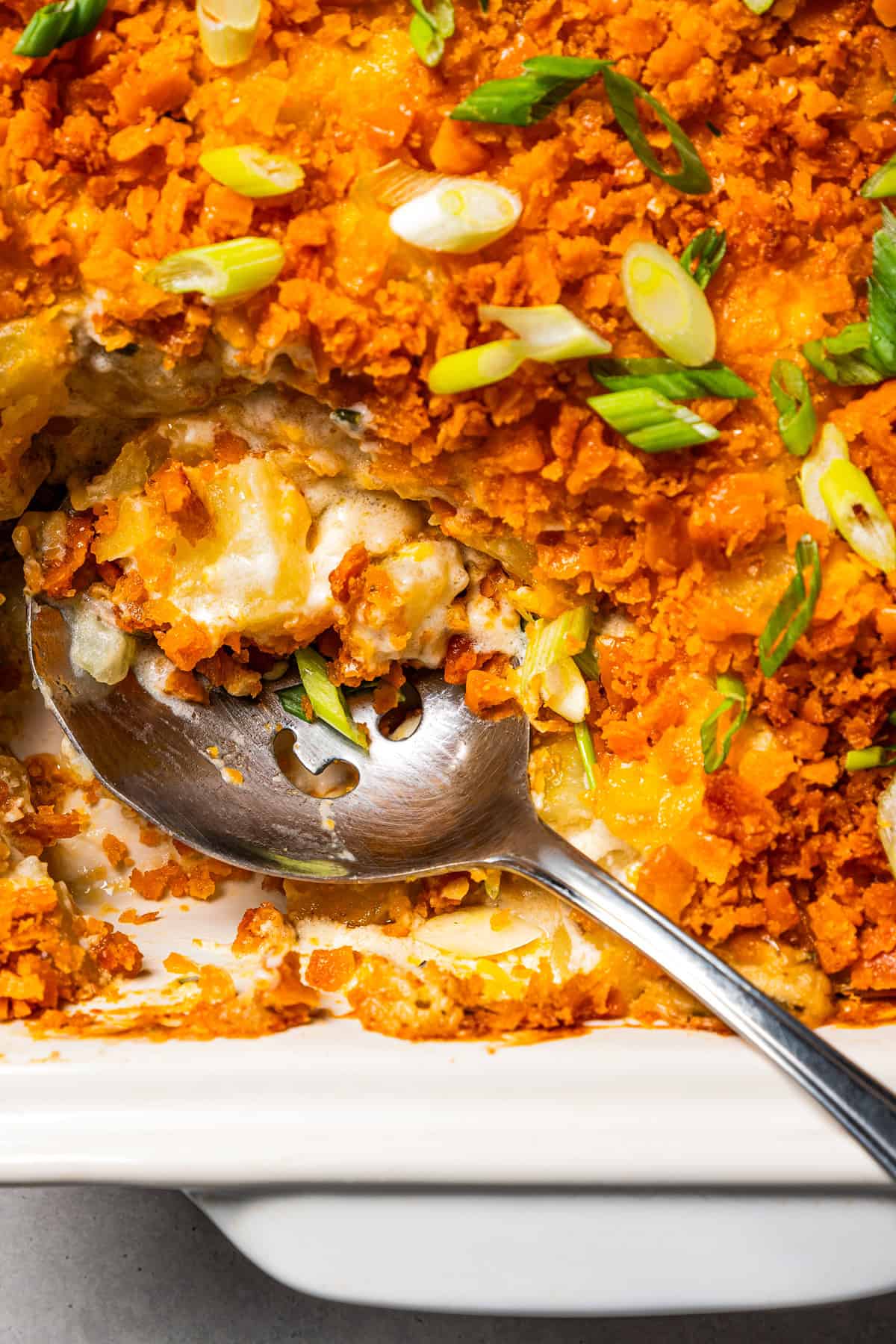 Baked cheesy potatoes in a baking dish with a scoop missing from the corner, and a serving spoon resting in the space.