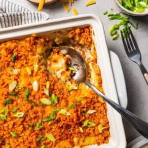 Overhead view of baked potatoes in a baking dish with a serving spoon scooping out the potatoes.