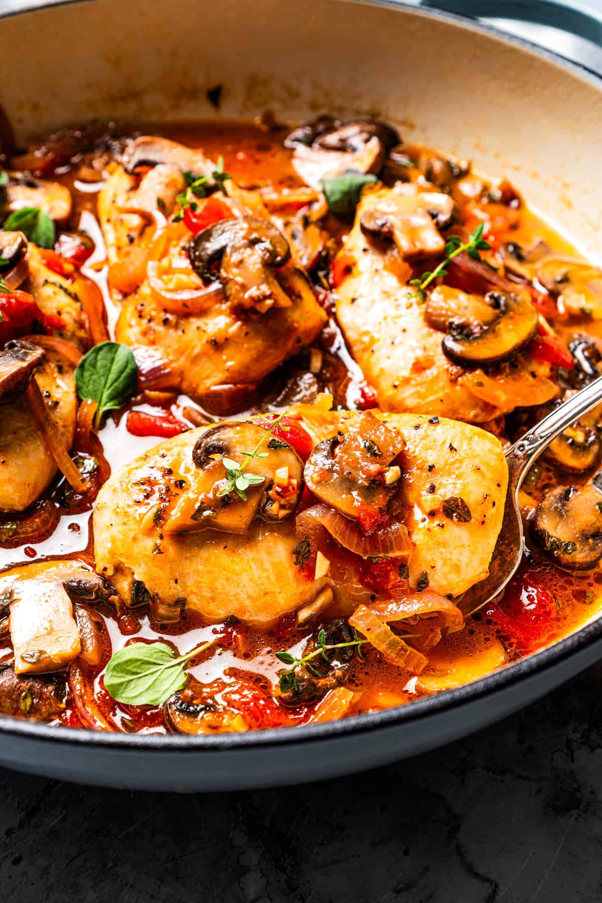 Serving spoon scooping out chicken chasseur from the skillet.