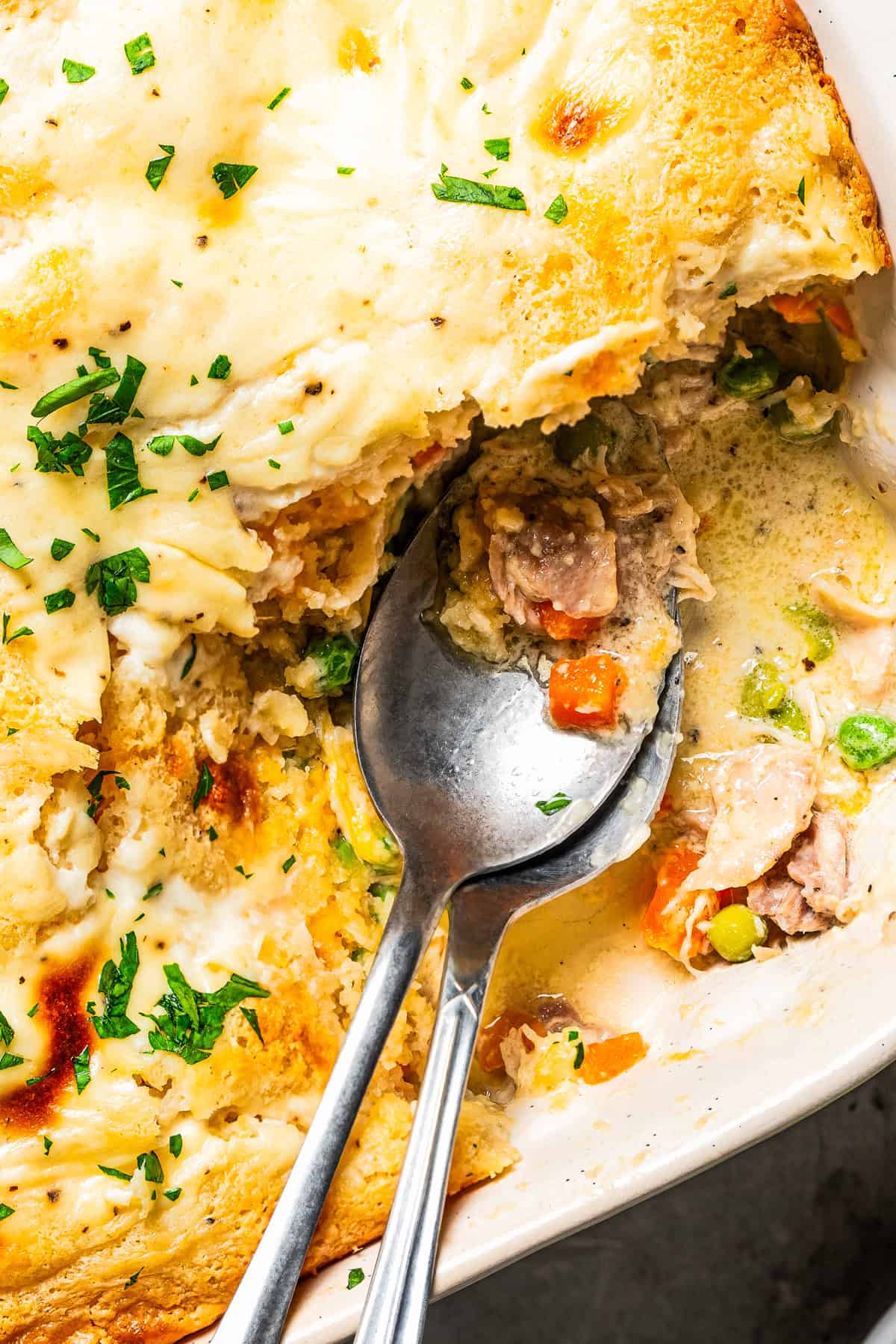 Close-up image of two serving spoons in a baking dish with a baked casserole.