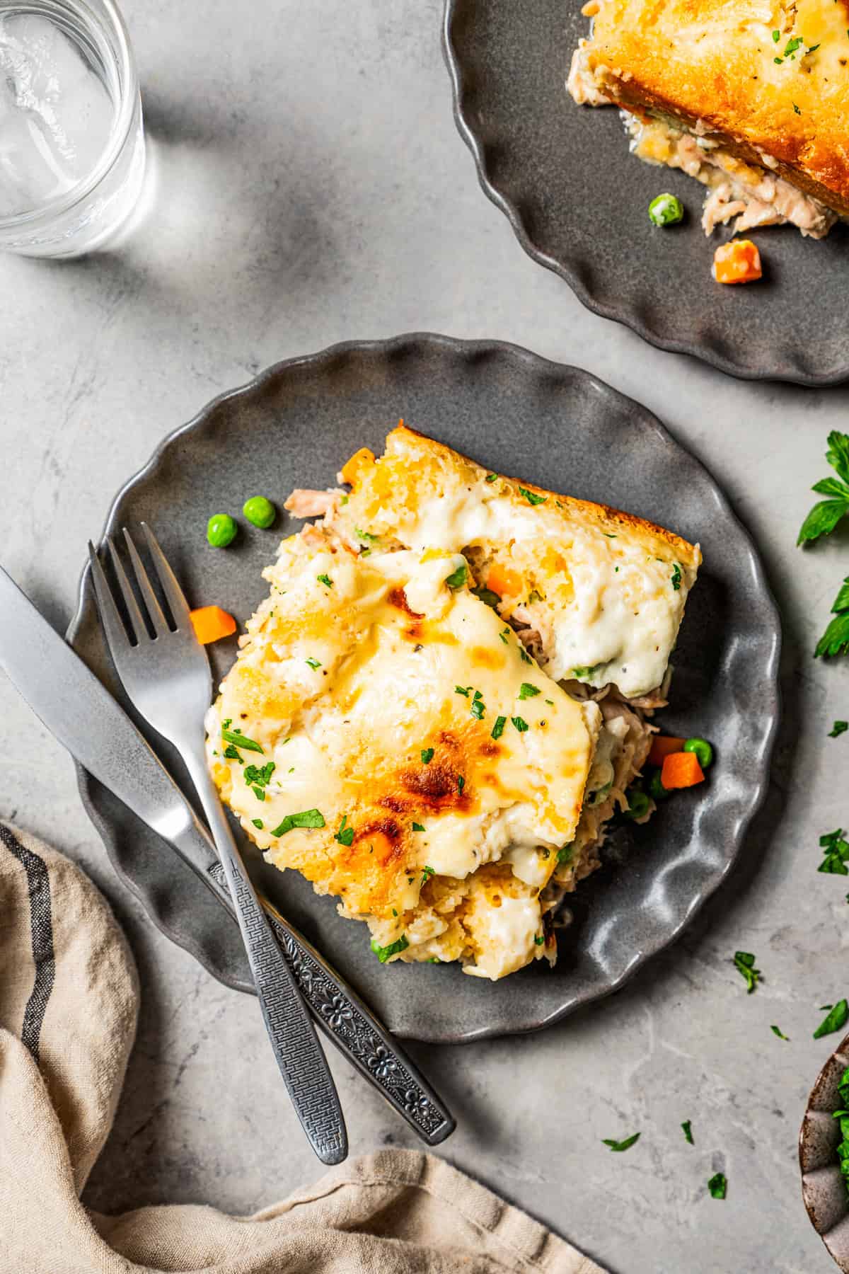 This chicken cobbler recipe combines a creamy chicken and veggie base with a buttery, cheesy biscuit layer and a creamy, bubbly topping. A scoop of chicken cobbler served on two dinner plates.