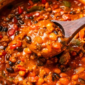 A wooden spoon scooping out pumpkin chili from a pot.