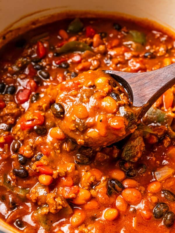 A wooden spoon scooping out pumpkin chili from a pot.