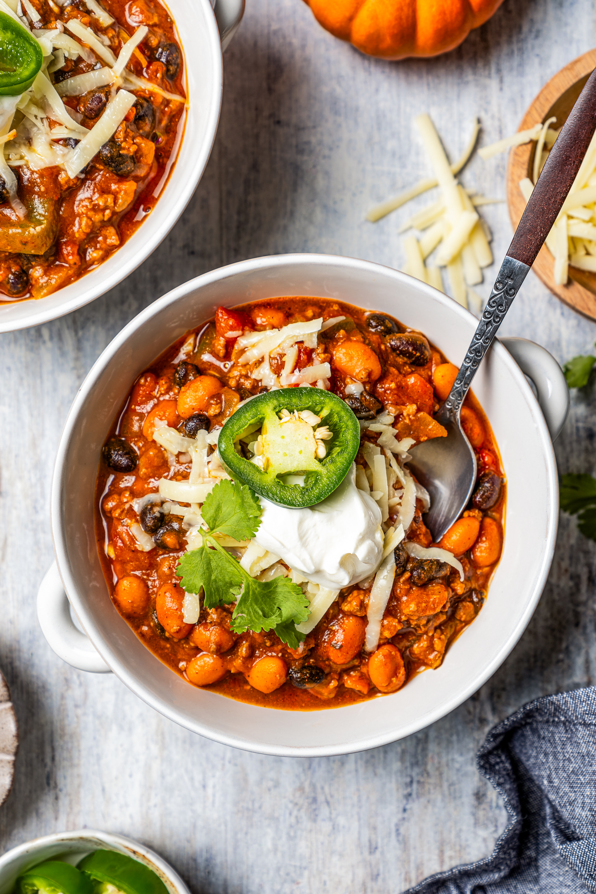 Overhead view of two bowls of pumpkin chili topped with sour cream and jalapeño slices.