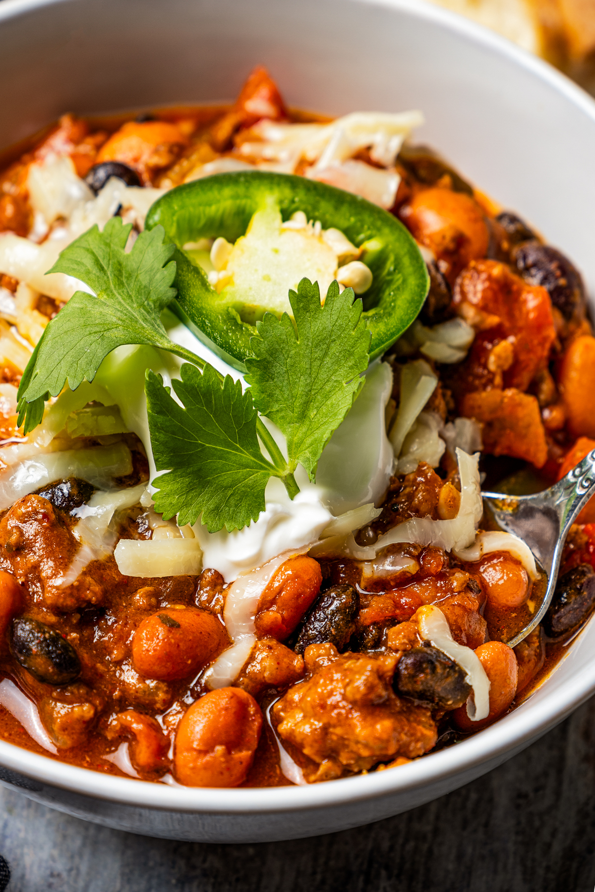 Close-up photo of pumpkin chili in a white bowl topped with sour cream and jalapeño slices.