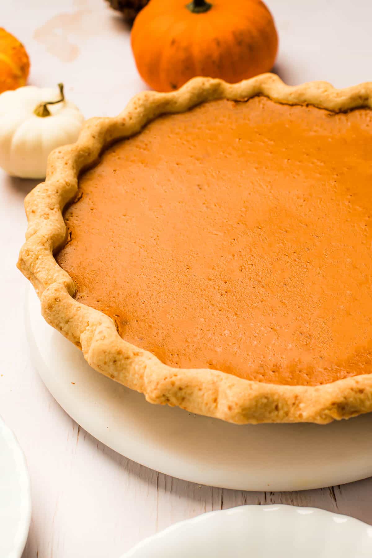 Whole homemade pumpkin pie set on a table next to small pumpkins.