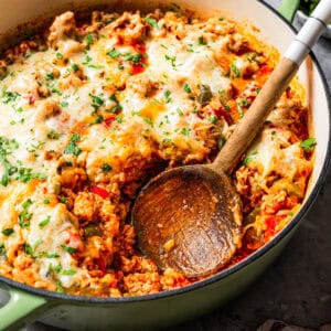 Wooden spoon resting in a baking dish with stuffed pepper casserole.