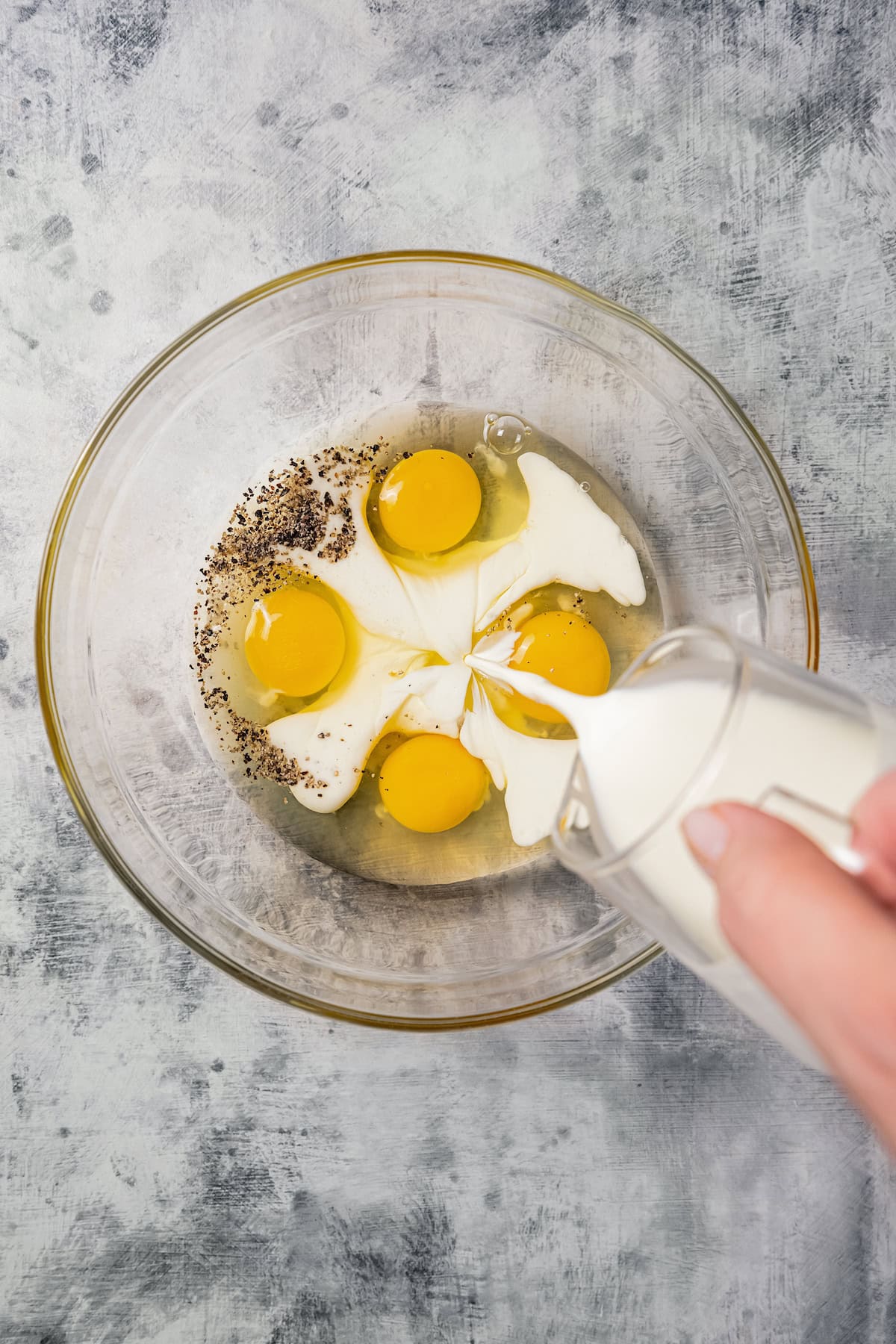 Milk poured over eggs in a glass bowl.