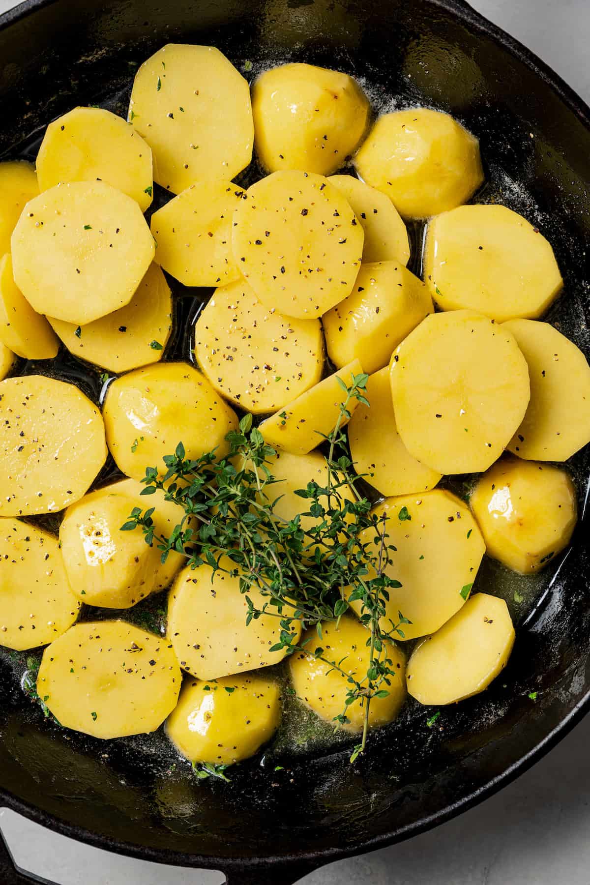 Sliced potatoes added to a skillet of melted butter, topped with thyme.