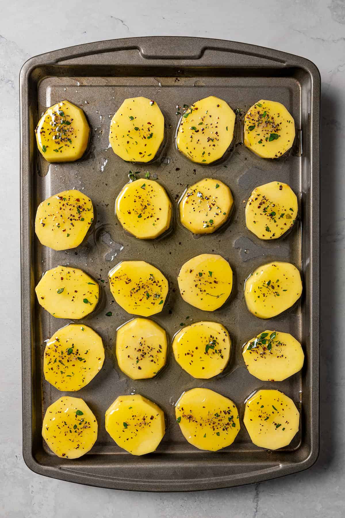 Seasoned potato slices arranged in rows on a baking sheet.