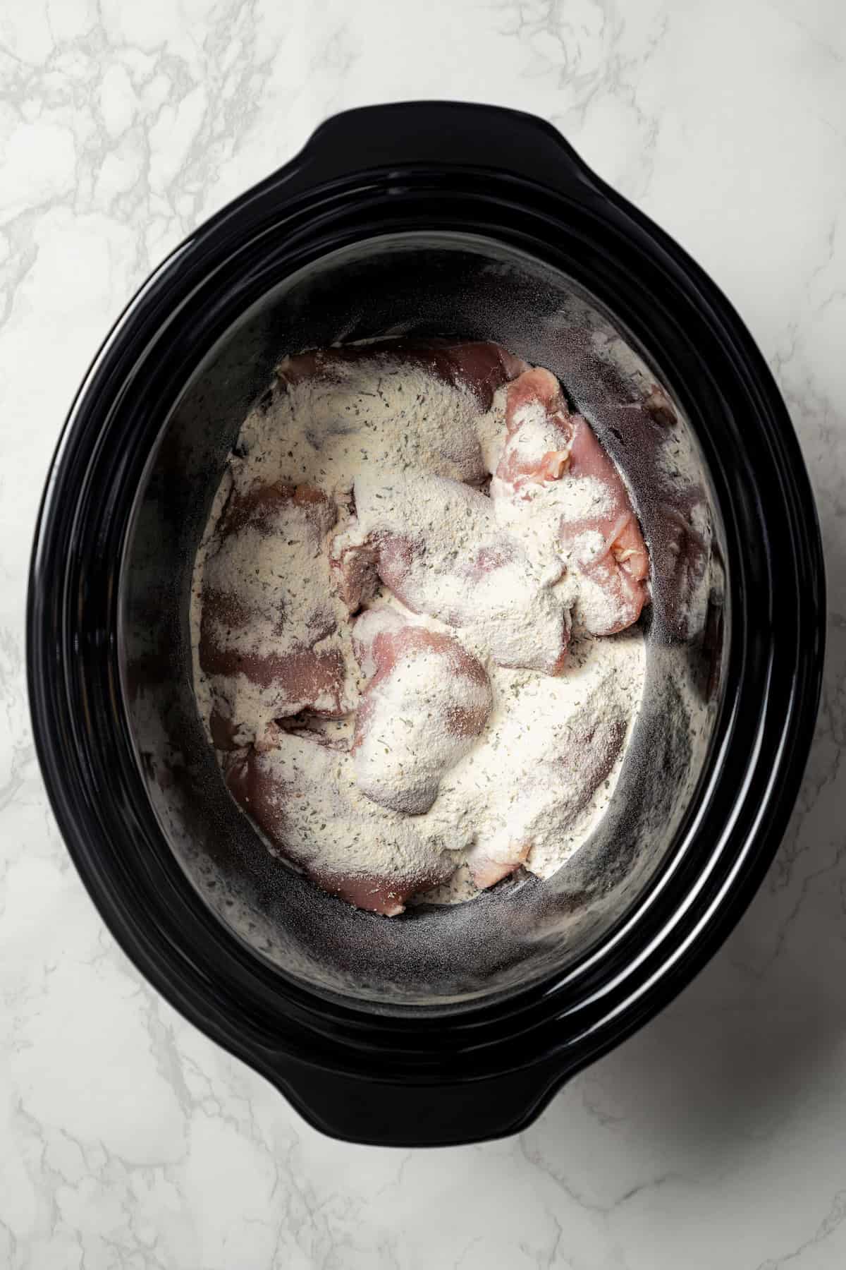 Chicken thighs topped with ranch mix and onion soup mix inside the slow cooker.