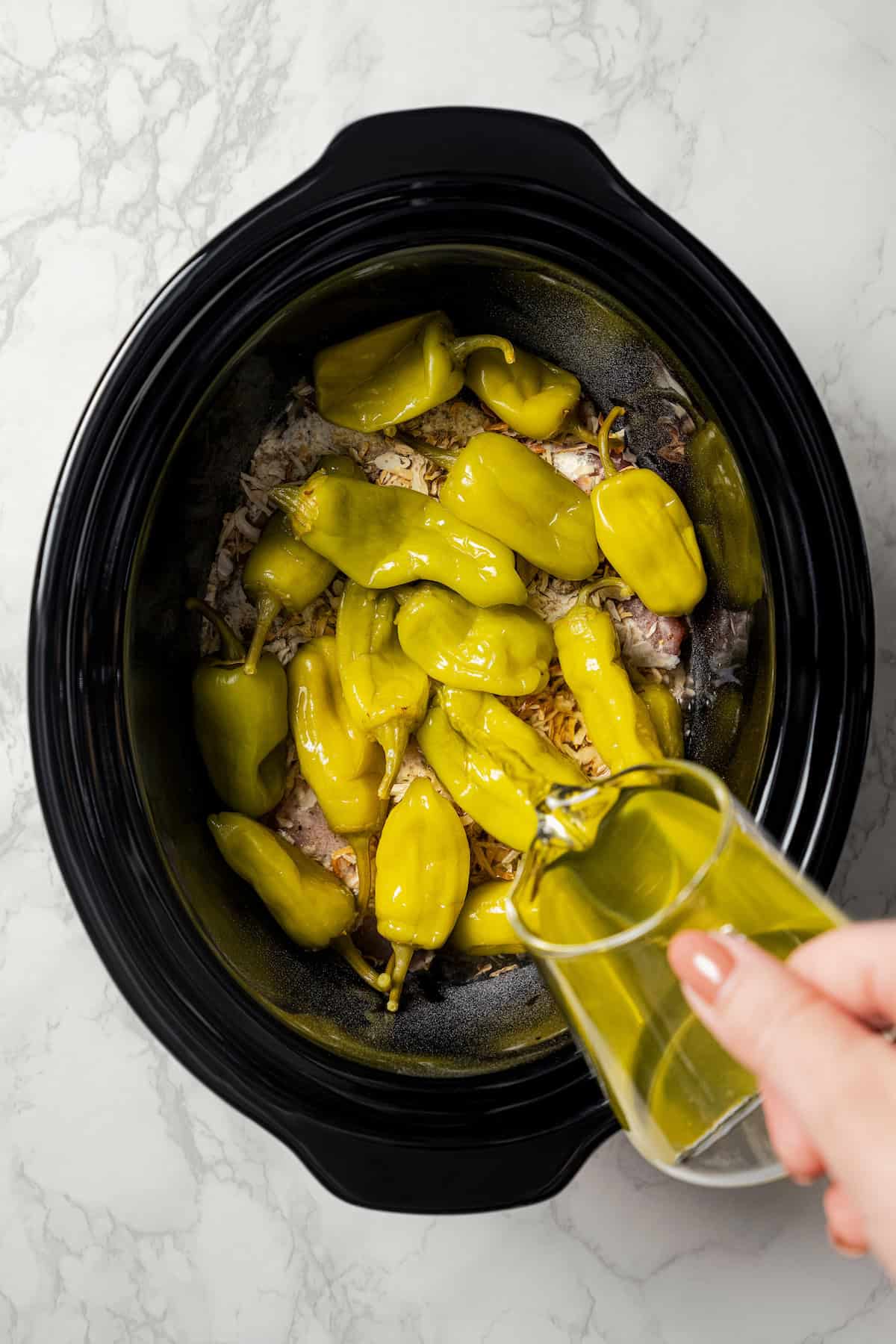 Pepperoncini juice being poured over the peppers and chicken inside the crock pot.