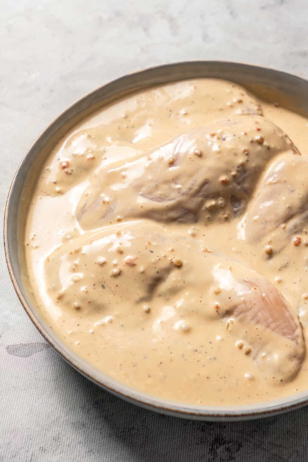 Chicken breasts soaking in a bowl of Italian chicken marinade.