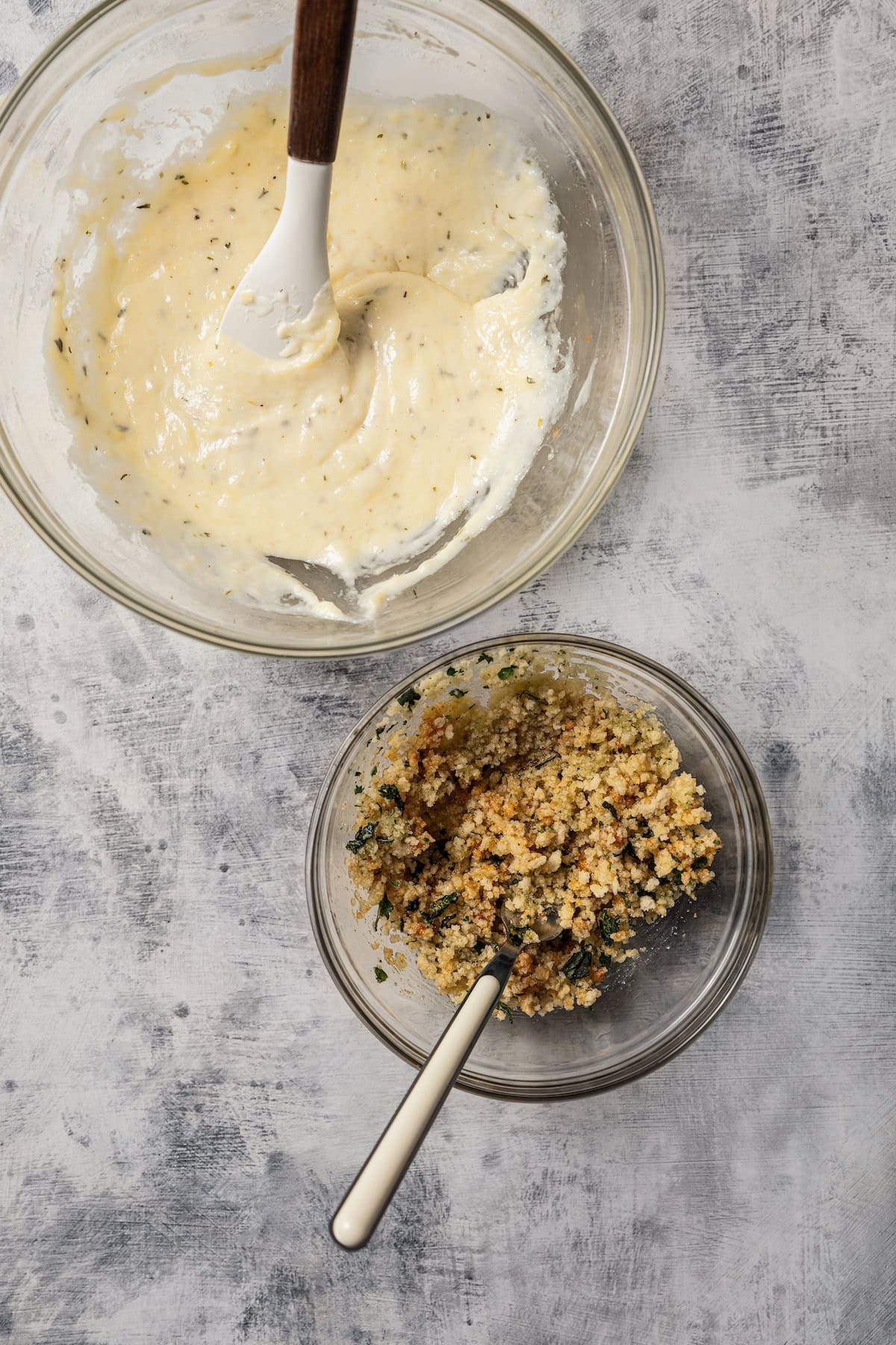 A bowl of parmesan sauce next to a smaller bowl of seasoned breadcrumbs.