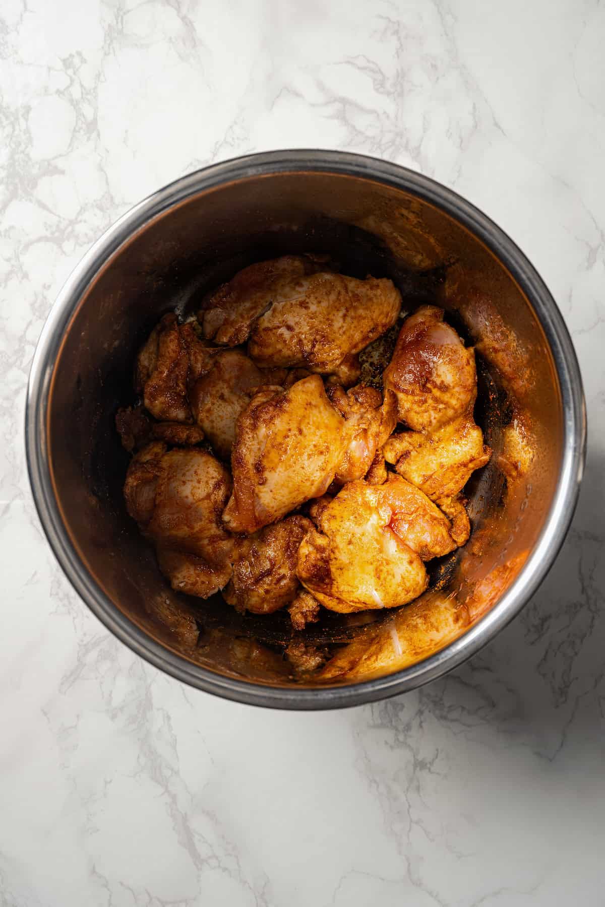 Seasoned chicken pieces in a metal bowl.