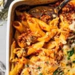 A serving spoon is scooping out mostaccioli from a casserole dish.