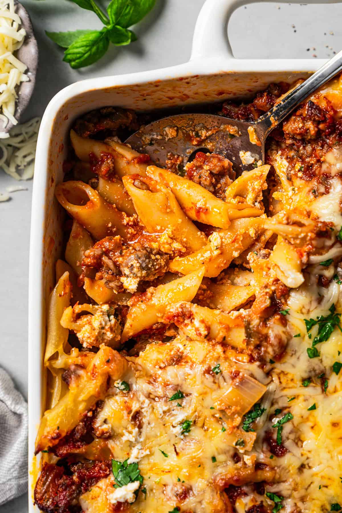 A serving spoon is scooping out mostaccioli from a casserole dish.