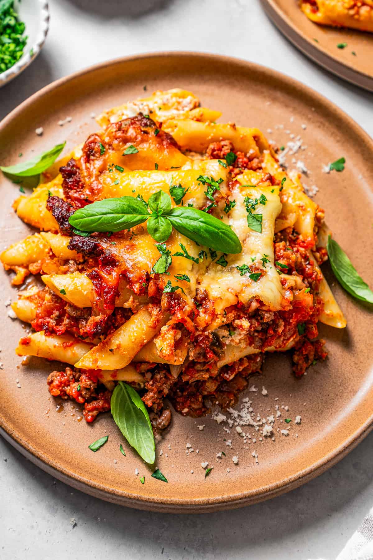 Serving of baked mostaccioli on a dinner plate, with a garnish of fresh basil.