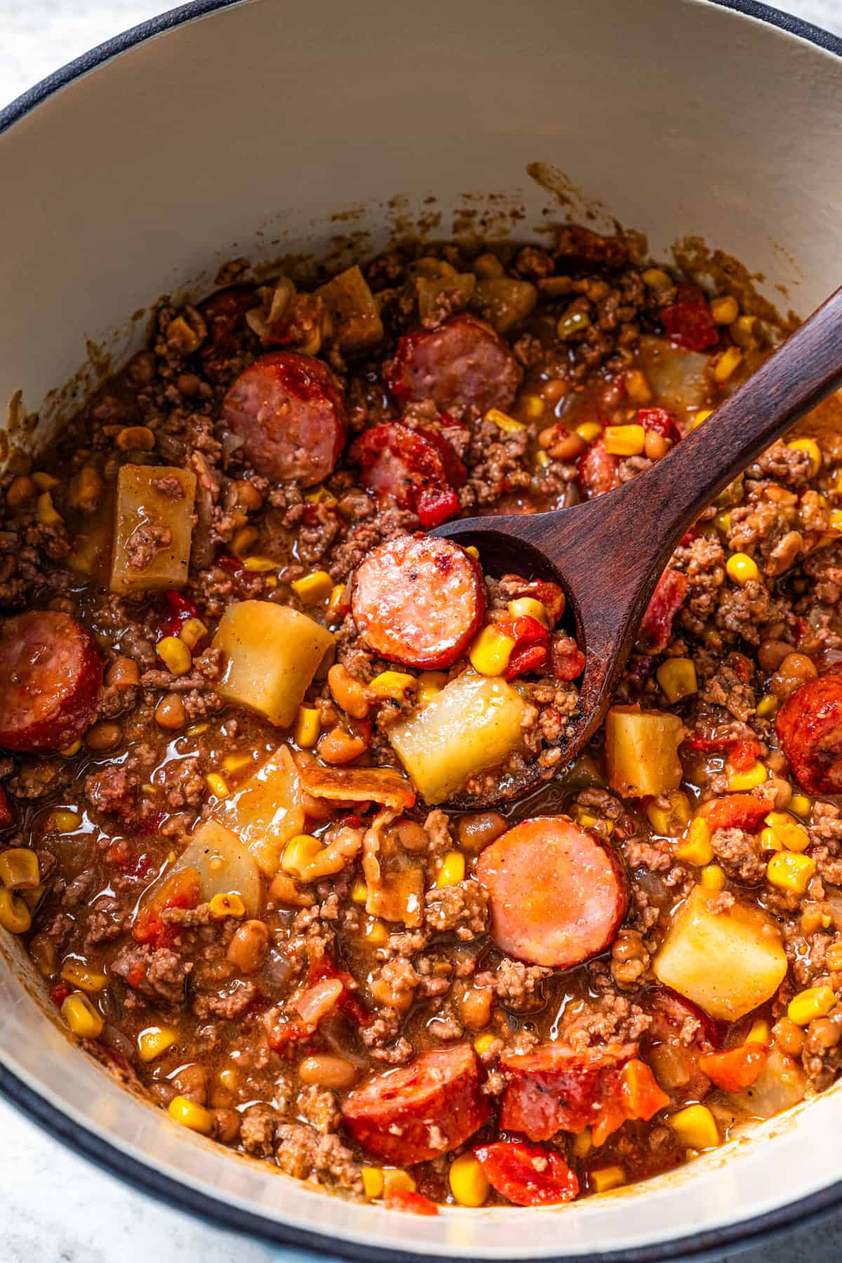 Cowboy stew in a soup pot with a wooden spoon stirring through.